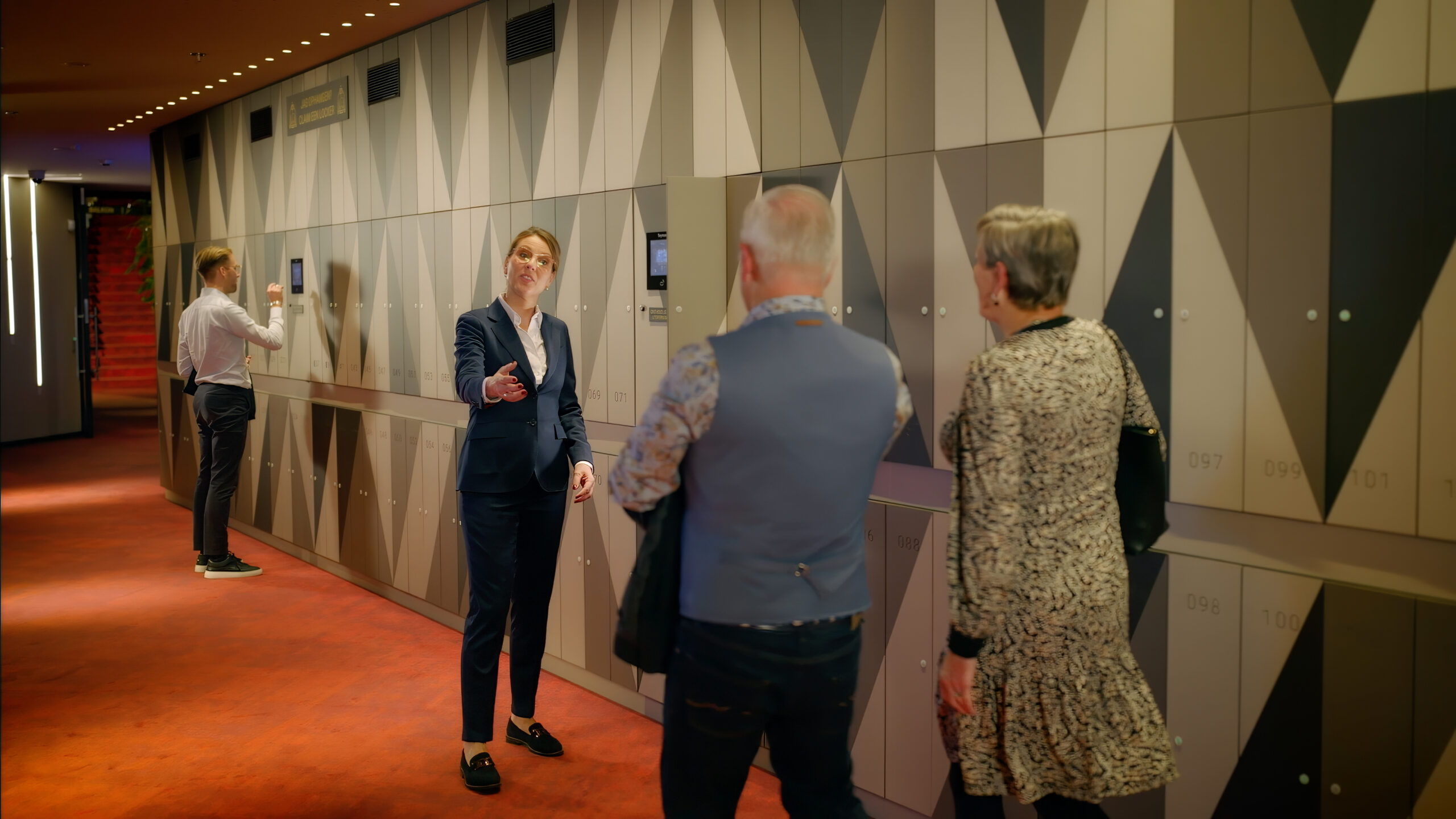 Een medewerkster van het AFAS Theater begeleid bezoekers naar de garderobe kluisjes van het theater.